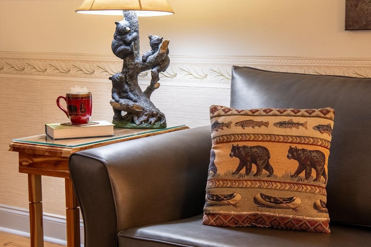 Um sofá de couro com uma almofada estampada, uma mesa com uma luminária e uma caneca, e um livro.