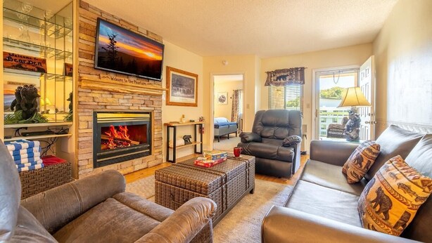 A living room with a fireplace, leather sofas, a television, and a bookshelf. - The Bears Den (Pigeon Forge)