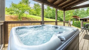 Un bain à remous situé dans un espace extérieur abrité, avec vue sur les arbres et une terrasse en bois.
