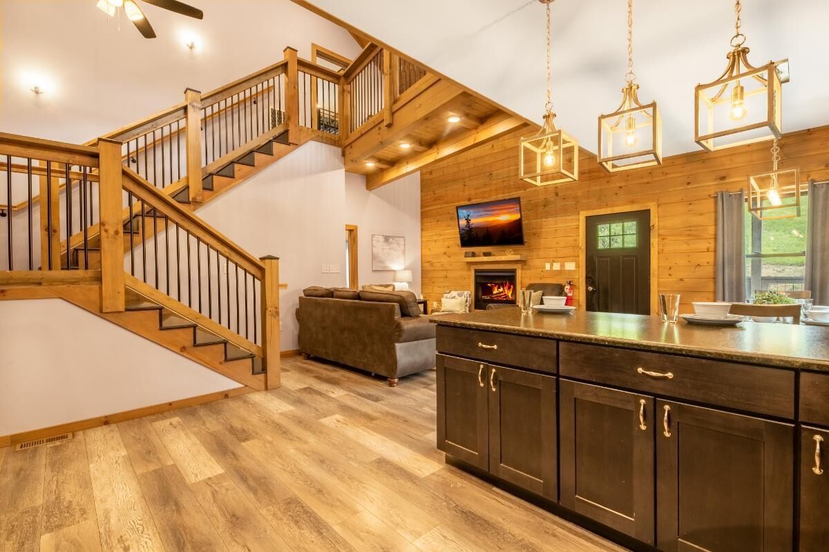 A modern kitchen with wooden cabinetry, a built-in island, a fireplace, and a staircase leading to an upper level.
