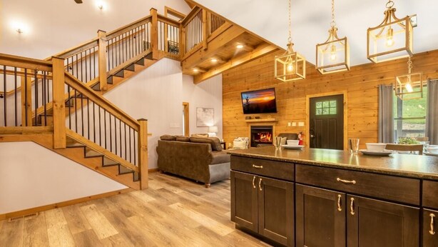 Une cuisine moderne avec des meubles en bois, un îlot central intégré, une cheminée et un escalier menant à l’étage supérieur.