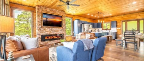 A cozy living room with a stone fireplace, blue sofas, a dining area, and a kitchen.