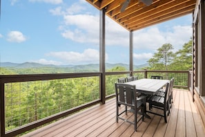 Eine Holzterrasse mit Tisch und Stühlen, mit Blick auf eine gebirgige Landschaft.