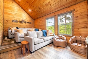 A cozy cabin interior with a sofa, bean bag chairs, and a window with a view of trees. - Redtail Horizon (Sevierville)