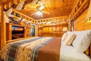 A wooden cabin interior with a bed, ceiling fans, a television, and a fireplace. - Awesome View (Sevierville)