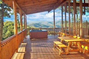 Um deck de madeira com hidromassagem, mesas de piquenique e uma vista panorâmica das montanhas.