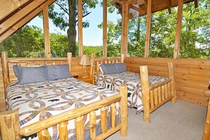 Uma cabana de madeira com duas camas, cada uma com roupa de cama estampada, e vista para árvores verdes.