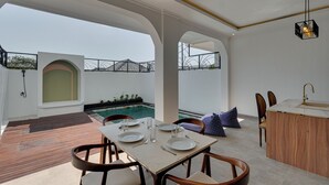 Un comedor con una mesa preparada para cuatro personas, una piscina al fondo y vistas del paisaje circundante.
