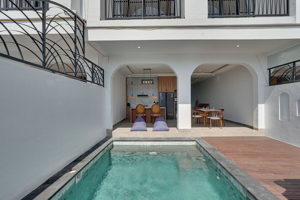 A modern pool area with a clear pool, wooden deck, and a dining area with chairs and a table.