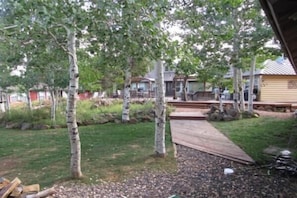 Ein Garten mit einer Holzterrasse, Bäumen und einem Haus im Hintergrund.