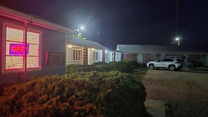 Un edificio con un letrero luminoso que dice 'OPEN', un SUV blanco estacionado adelante y un césped bien cuidado.