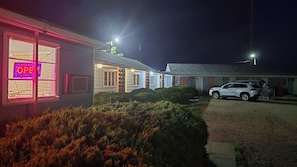 Un edificio con un letrero luminoso que dice 'OPEN', un SUV blanco estacionado adelante y un césped bien cuidado.