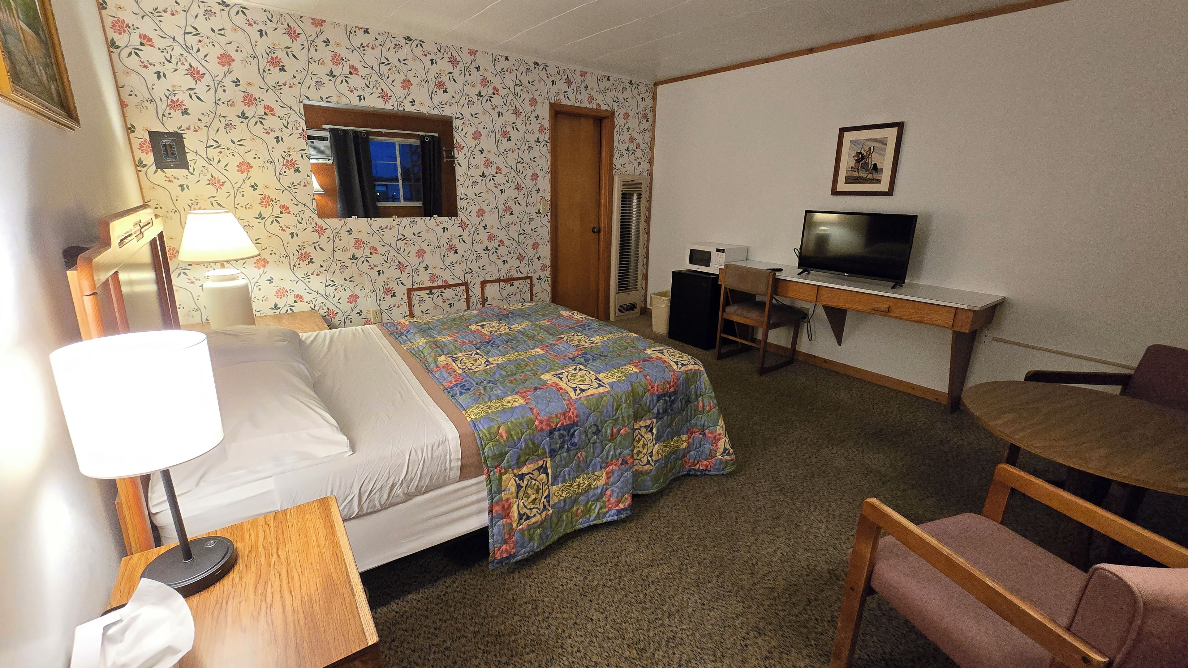 A hotel room with a bed, a desk with a television, a chair, and a carpeted floor.