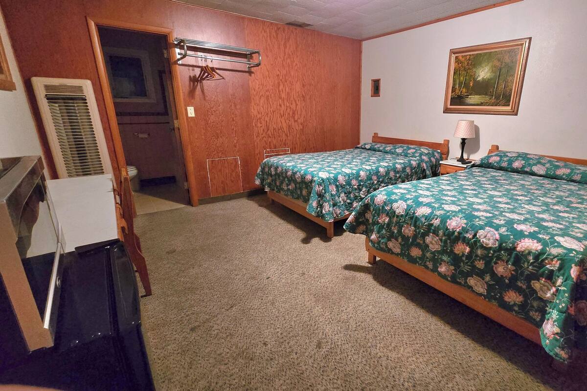 Un dormitorio con dos camas, un armario de madera, un radiador y un cuadro en la pared.
