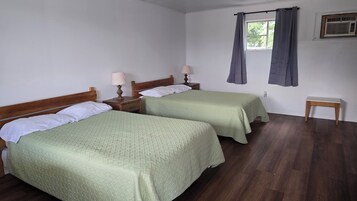 Una habitación con dos camas, una mesita pequeña, un ventanal con cortinas y un aire acondicionado instalado en la pared.