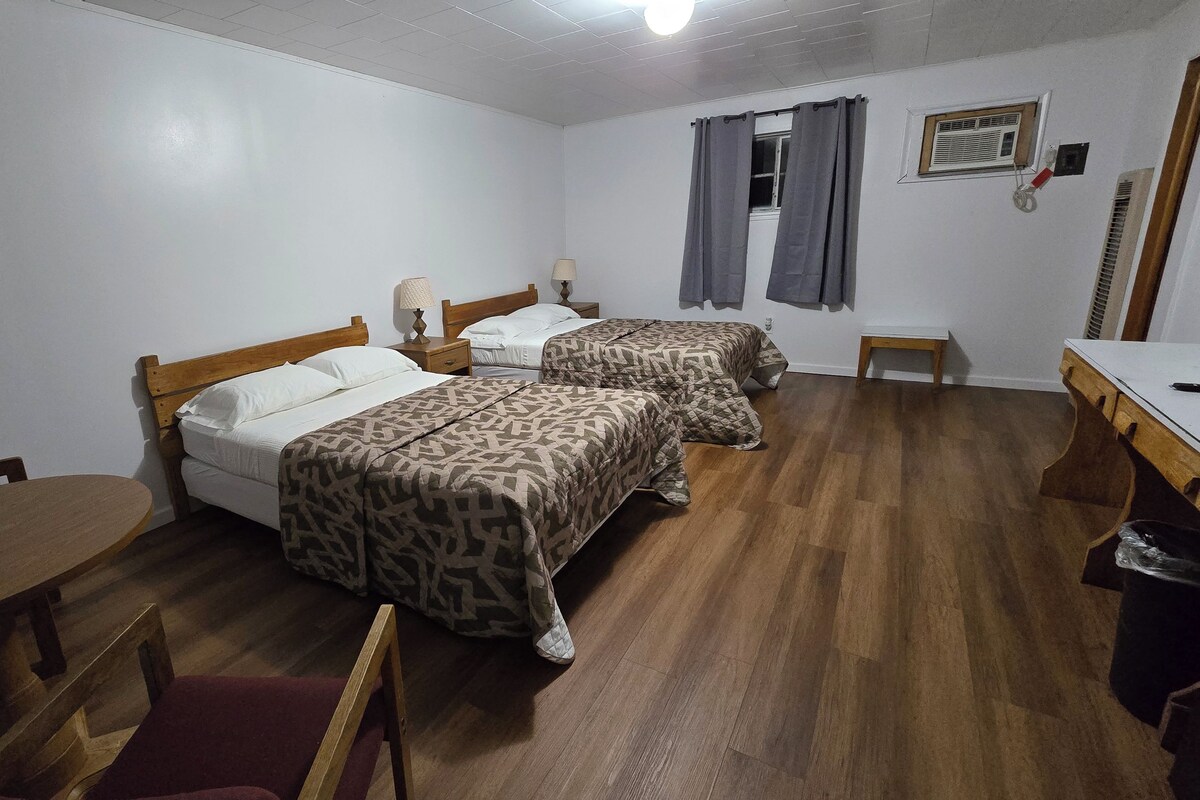 A room with two beds, a desk, a chair, and a small table.