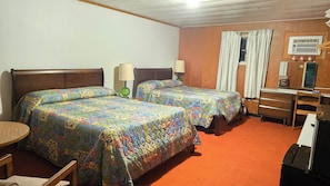 Habitación de hotel con dos camas, un escritorio, una silla, una lámpara, un calefactor y una ventana con cortinas.