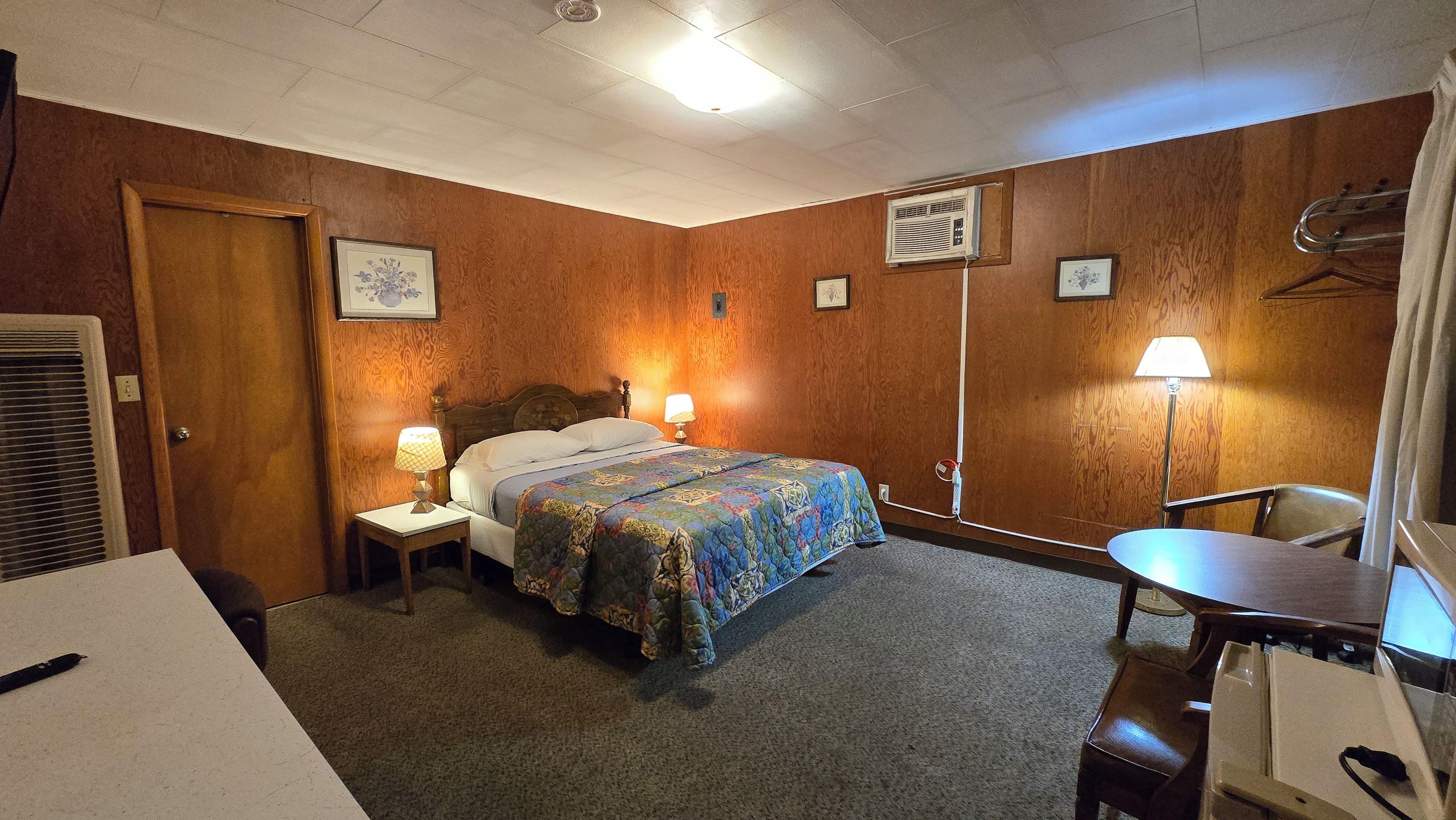 Una habitación de hotel con una cama, lámparas de noche, un escritorio y una silla.