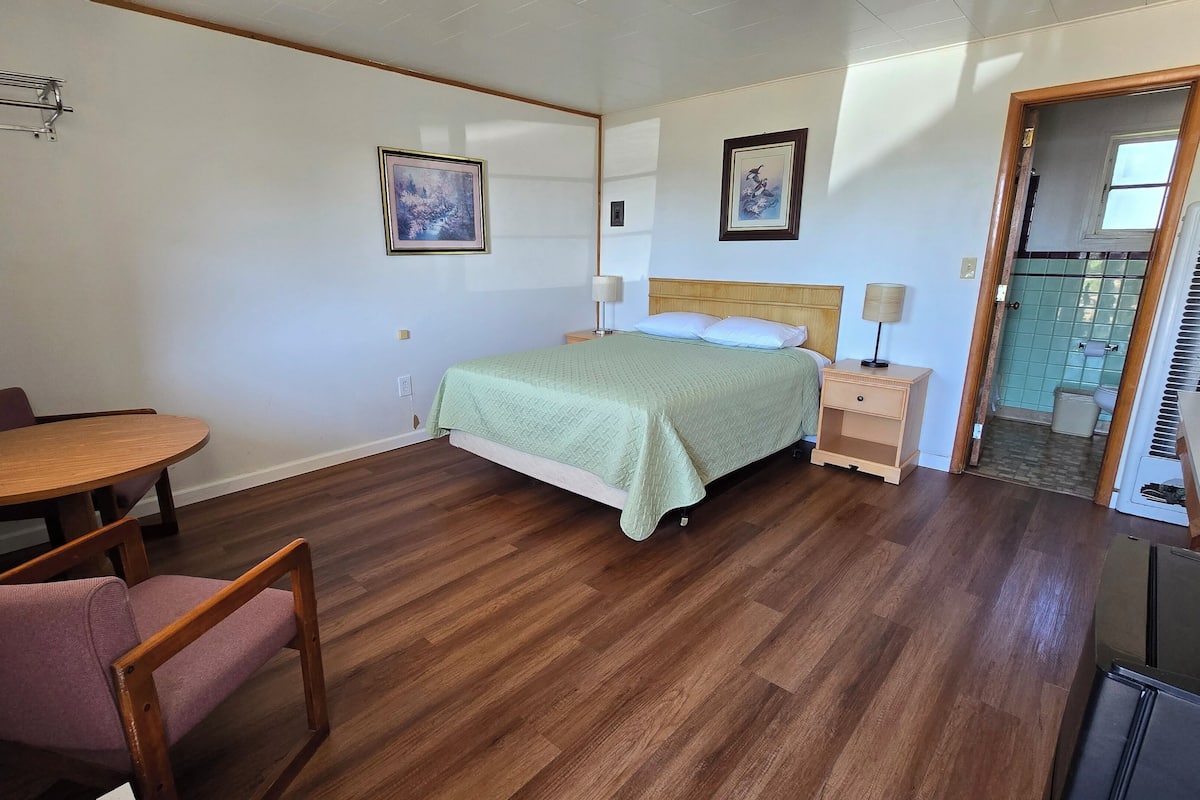 Una habitación con cama, una mesa y sillas, una ventana y una puerta que da a un baño.
