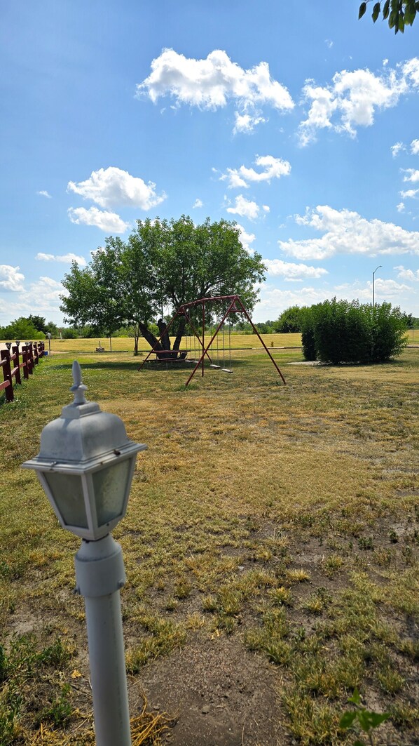 A park with a swing set, a lamp post, and a tree. - Lazy K Motel (Ogallala)