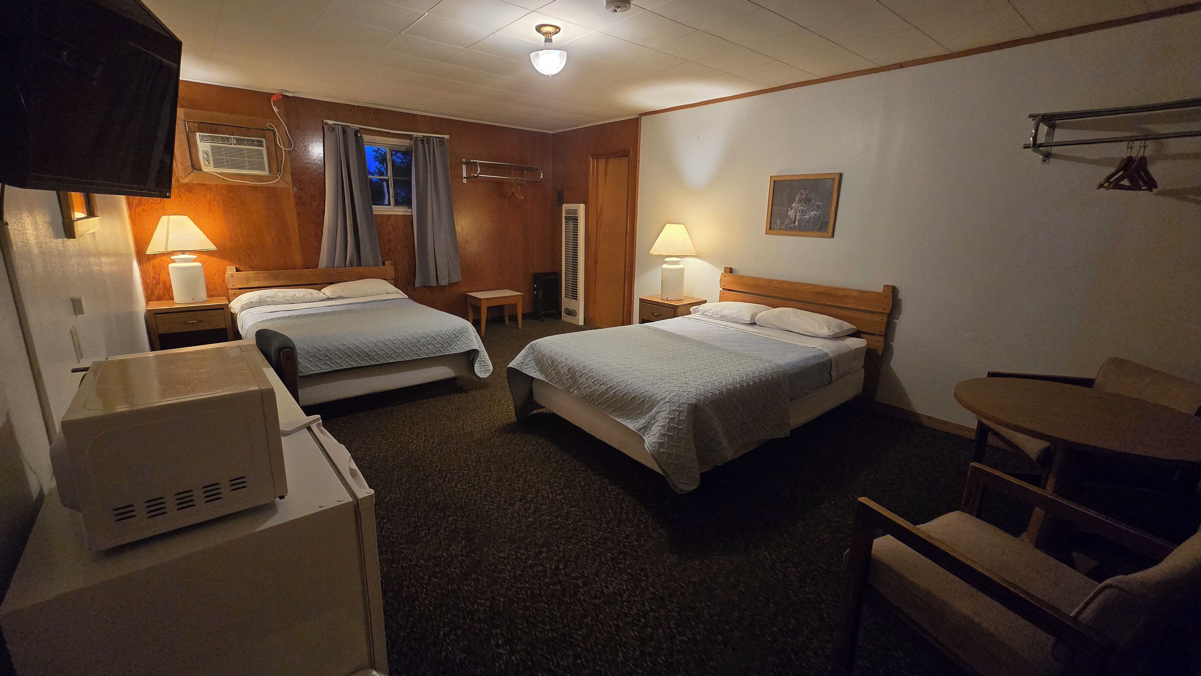 Habitación de hotel con dos camas, un escritorio, una silla, una lámpara y un cuadro en la pared.
