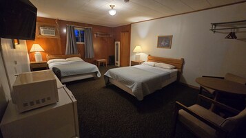 Habitación de hotel con dos camas, un escritorio, una silla, una lámpara y un cuadro en la pared.