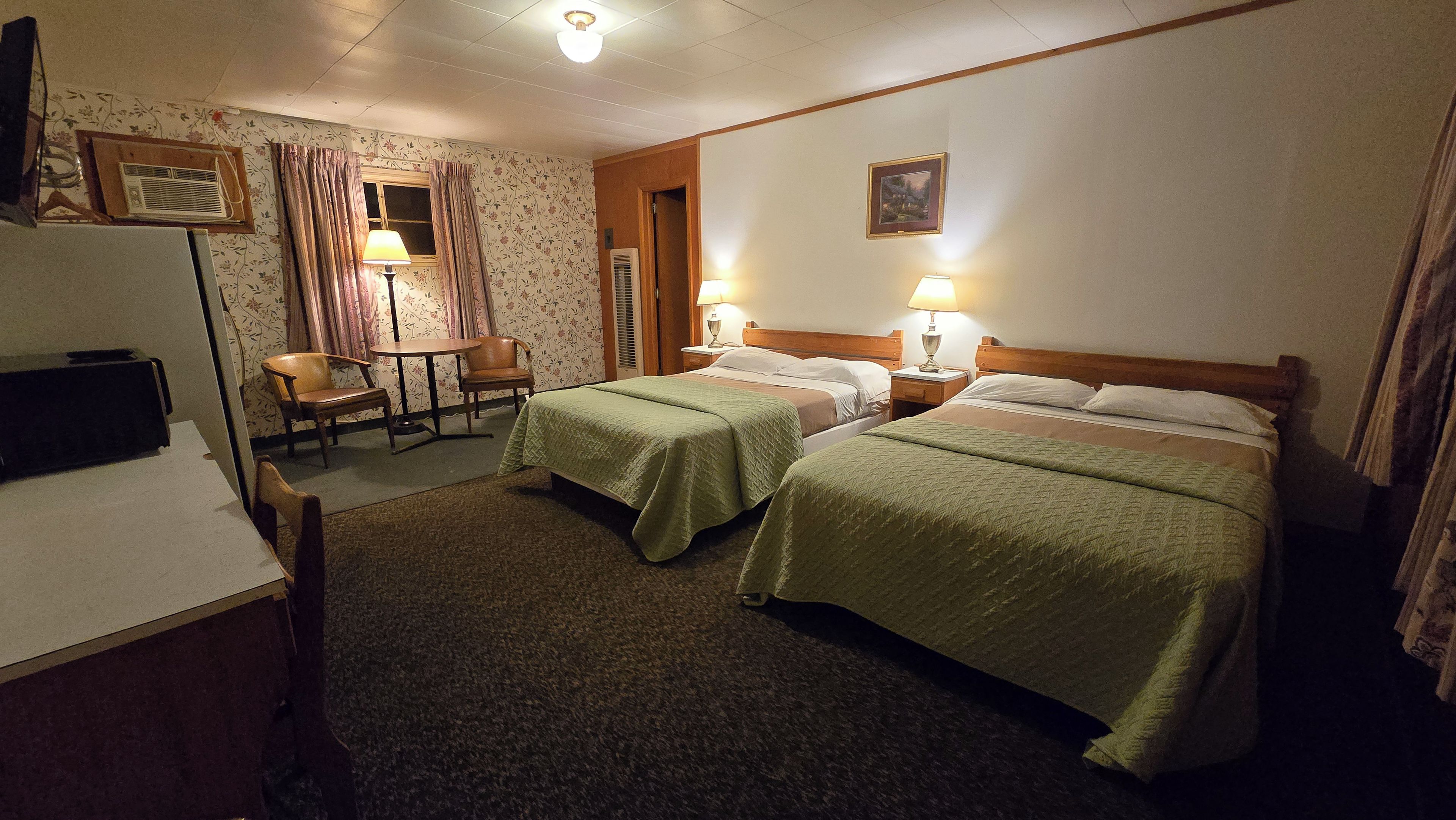 A hotel room with two beds, a desk, a chair, a lamp, and a picture on the wall.