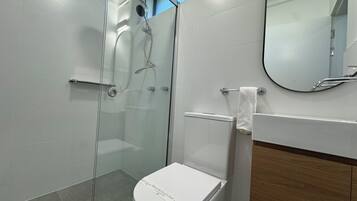 A modern bathroom with a glass-enclosed shower, a toilet, and a mirror.