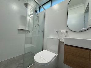 Un baño moderno con ducha envuelta en vidrio, inodoro y espejo.