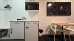 Una kitchenette compacta con microondas, un refrigerador pequeño y una mesa de madera con sillas.