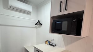 Una kitchenette compacta equipada con microondas, un refrigerador pequeño y una encimera blanca.