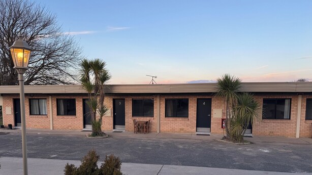 Motel con fachada de ladrillo, puertas numeradas y un pequeño patio con mesa y sillas.