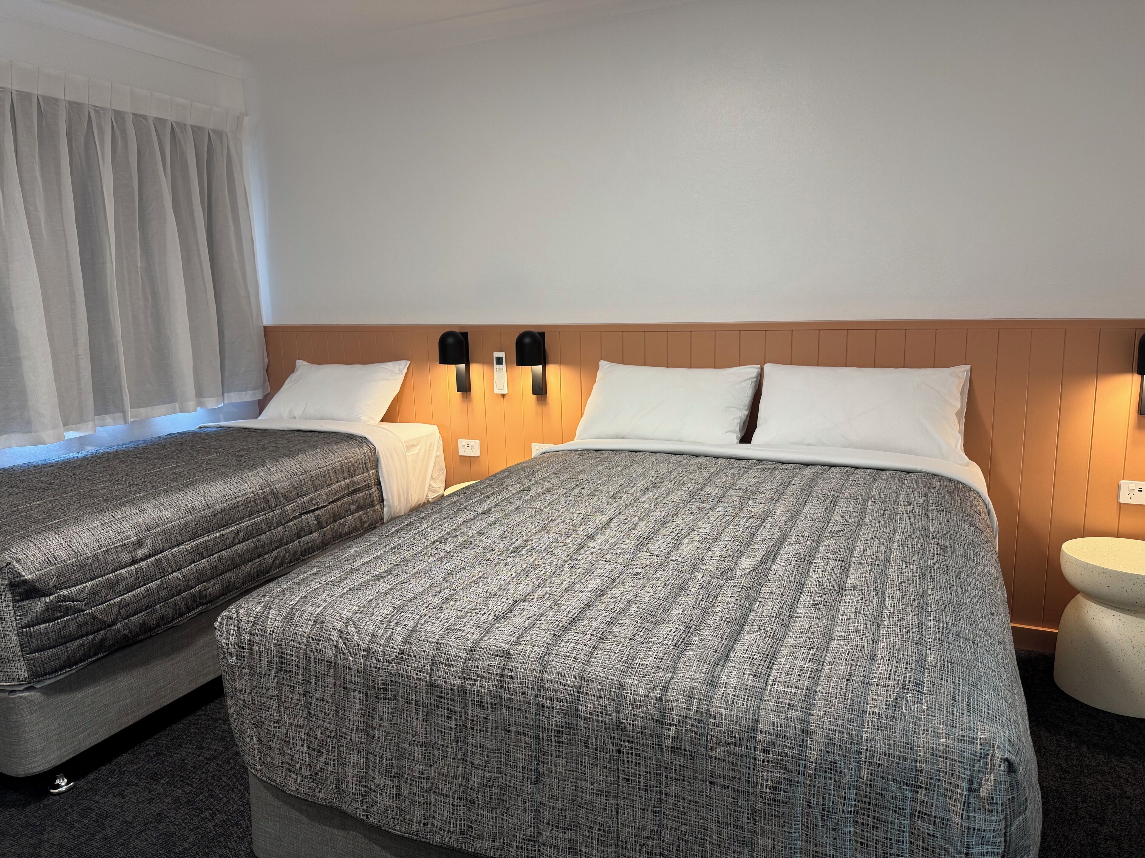 A hotel room with two beds, a wooden headboard, bedside lamps, and a round bedside table.