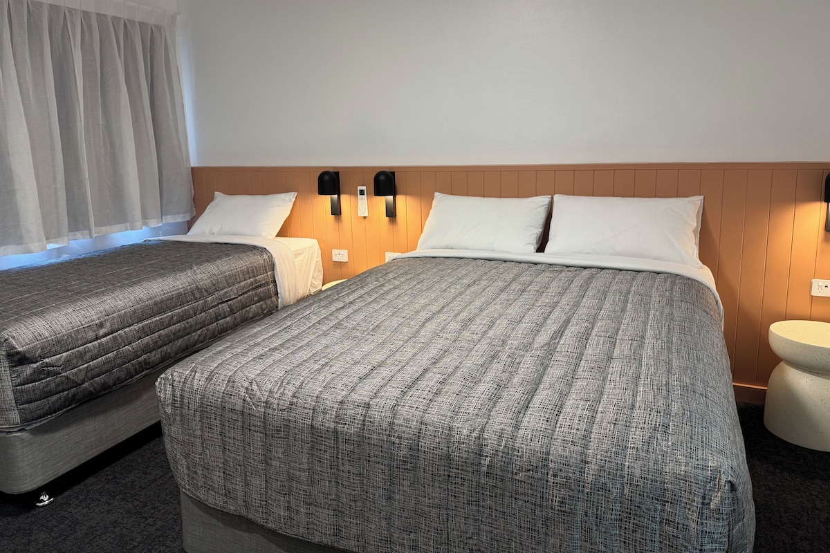 Habitación de hotel con dos camas, cabecero de madera, lámparas de noche y una mesita redonda.