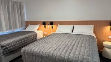 A hotel room with two beds, a wooden headboard, bedside lamps, and a round bedside table.