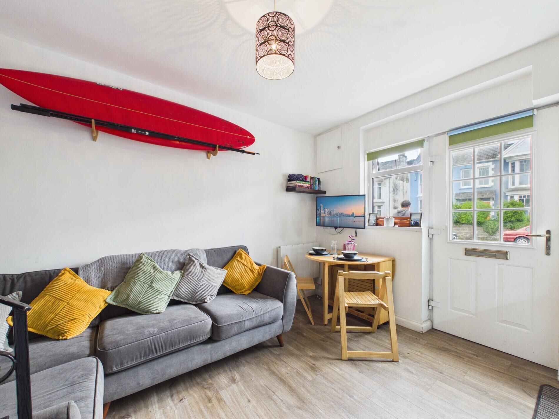 Un salón con un sofá gris, una silla de madera y una tabla de surf roja en la pared.