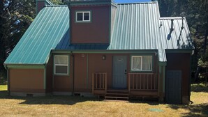 A single-story house with a green metal roof, a front porch, and a small front yard.