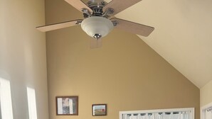 A living room with a ceiling fan, two armchairs, a sofa, a fireplace, and a window with curtains.