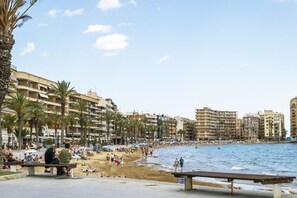 A beach with palm trees, a sandy shore, and buildings in the background. - Pink Harmony Apartment (Torrevieja)