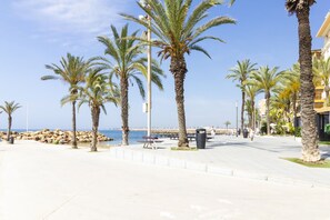 Eine Uferpromenade mit Palmen, wolkenlosem Himmel und Blick aufs Meer.