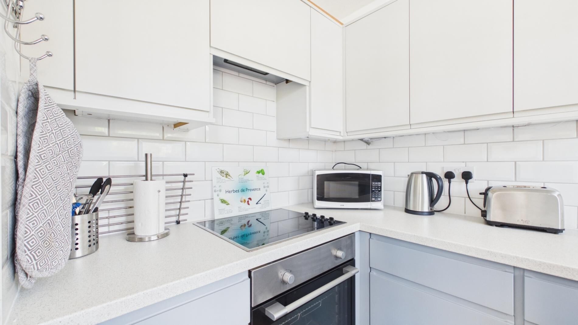 Een moderne keuken met witte kastjes, een magnetron, waterkoker, broodrooster en een gasfornuis.