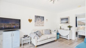 A modern living room with a sofa, TV, and artwork on the walls. - Bayview 62 - 2 Bedroom Chalet - Bayview Oxwich (Swansea)