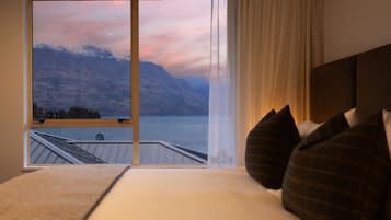 Ein Schlafzimmer mit einem großen Fenster, das Blick auf einen See und Berge gewährt.