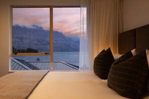 Ein Schlafzimmer mit einem großen Fenster, das Blick auf einen See und Berge gewährt.