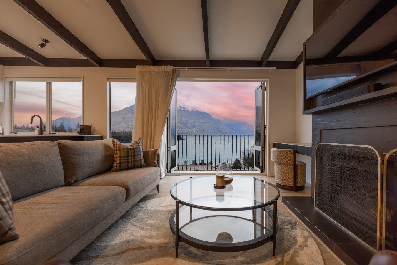 A living room with a sofa, a glass coffee table, a fireplace, and a view of mountains through large windows.