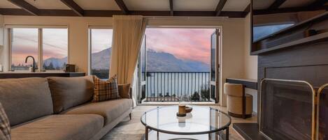 A living room with a sofa, a glass coffee table, a fireplace, and a view of mountains through large windows.