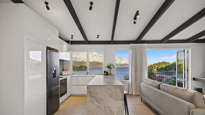 Una cocina moderna con una isla de mármol, un comedor con sofá y vistas a un lago y montañas.
