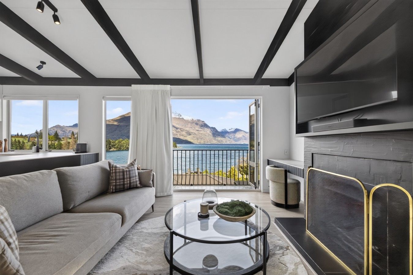 Ein modernes Wohnzimmer mit einer Couch, einem Couchtisch und einem Kamin. Ein Balkon bietet Blick auf das Meer und die Berge.