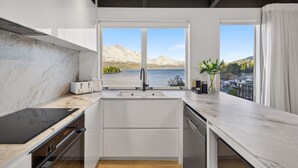 Una cocina moderna con un ventanal grande, vista a un lago y una montaña al fondo.