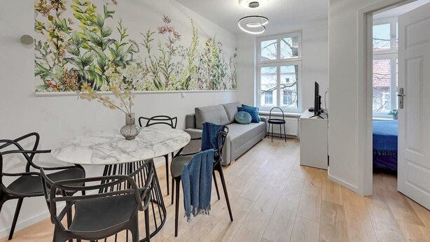 Ett modernt vardagsrum med en matplats, en soffa och en stor väggmålning med botaniska motiv.